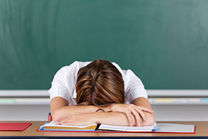 Stressed teacher with head on desk after working long hours