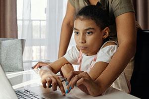A girl uses a laptop with help from mother – Cypher Learning