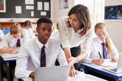 A pupil using a laptop with a teacher looking over his shoulder