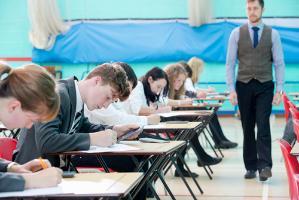 Children sitting an exam with a teacher watching on