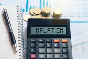 A calculator with the word inflation on it beside a pile of coins and a workbook
