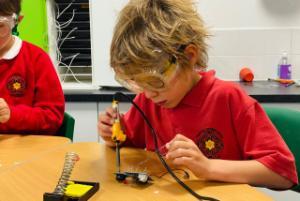 A young boy at school doing some soldering of a circuit board