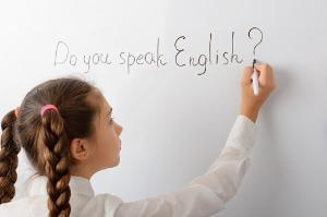 A child writing on a white board 'Do you speak English?'